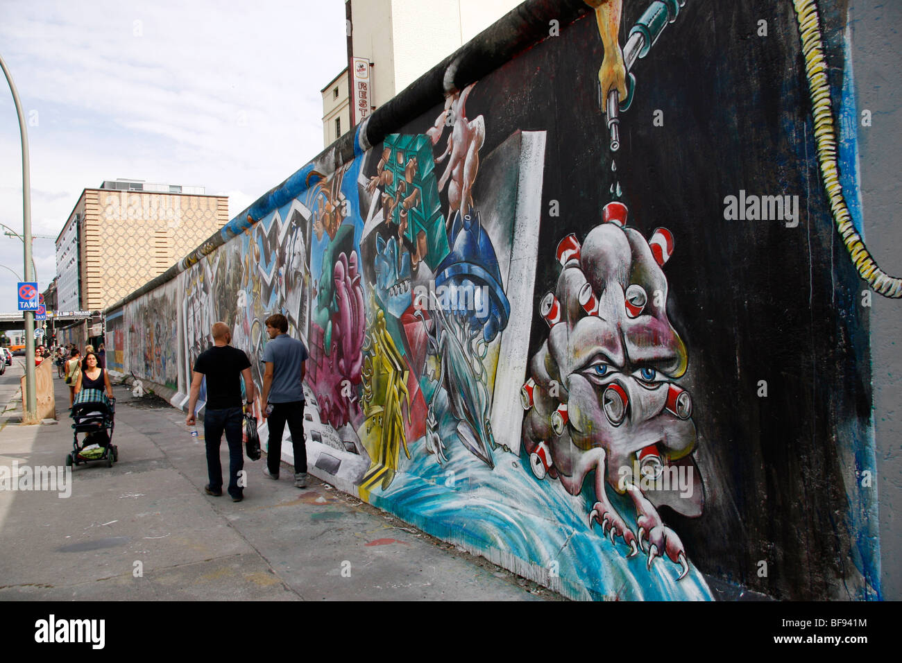 Fußgänger zu Fuß ging die Berliner Mauer an der East Side Gallery, einem 1,3 km langen Abschnitt der Mauer in der Nähe von Berlin Mitte. Stockfoto