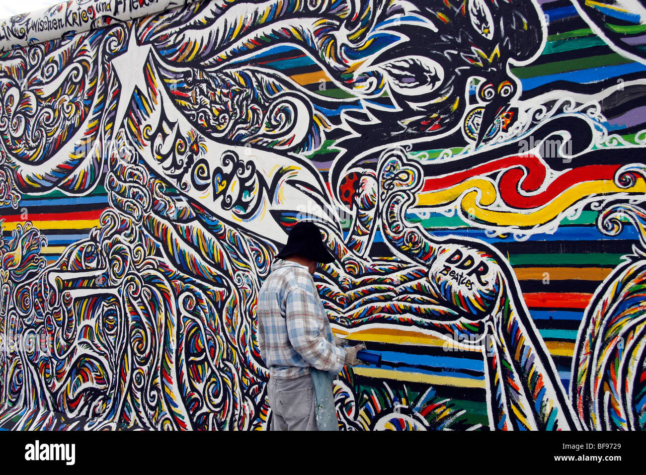 Ein Künstler malt die Berliner Mauer an der East Side Gallery, einem 1,3 km langen Abschnitt der Mauer nahe dem Zentrum von Berlin. Stockfoto