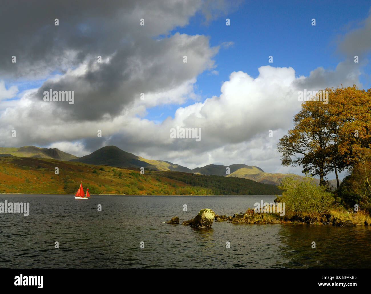 Ein rotes segelte Segelboot auf Coniston Water im englischen Lake District, mit Bergen im Hintergrund. Stockfoto