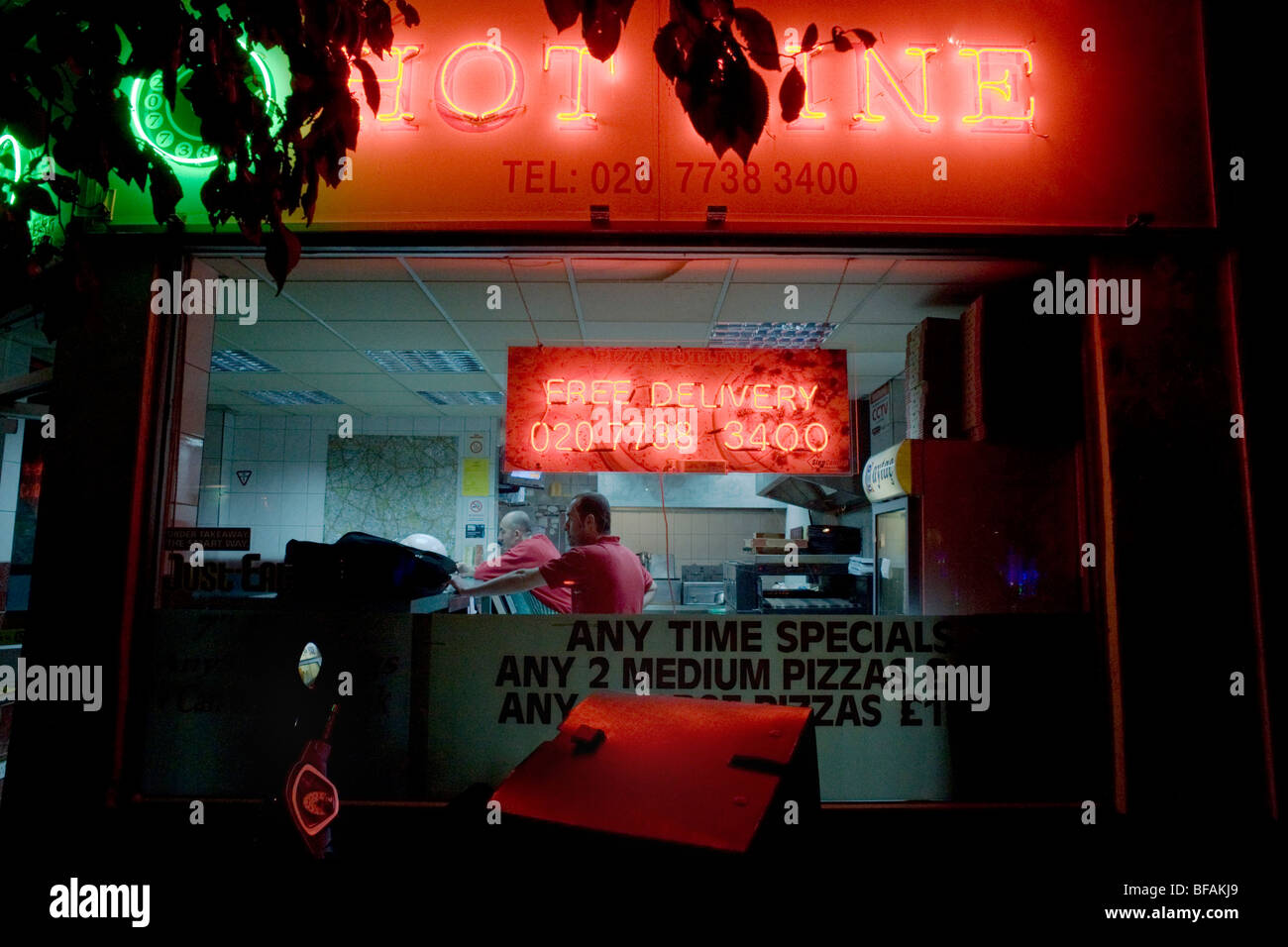 Leuchtenden Neonröhren und Mitarbeiter durch Fenster nachts eine Take-away Pizza-Geschäft in Herne Hill, London. Stockfoto