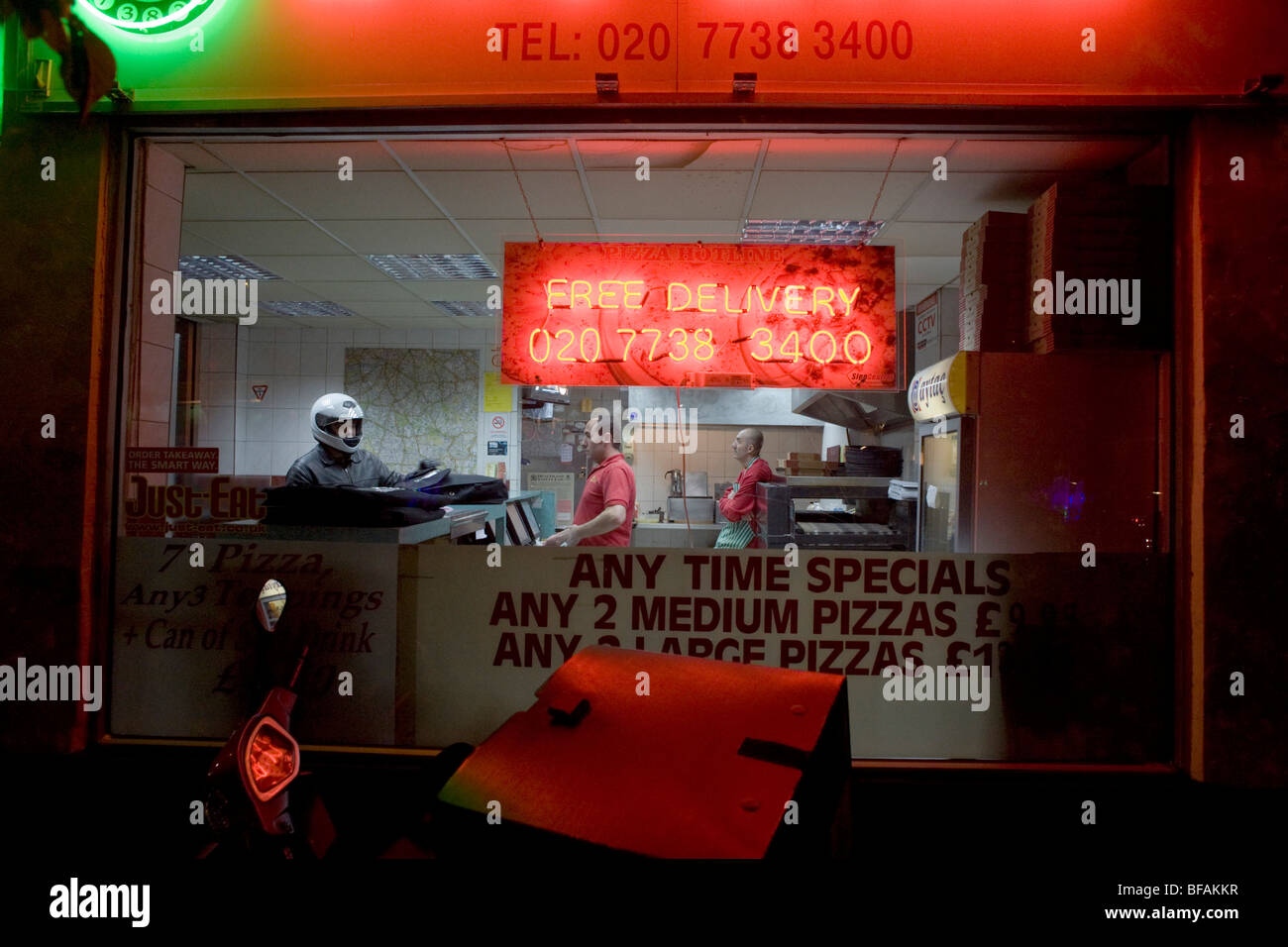 Ein Lieferung Fahrer sammelt Aufträge in der Nacht bei einem Take-away Pizza-Geschäft in Herne Hill, London. Stockfoto