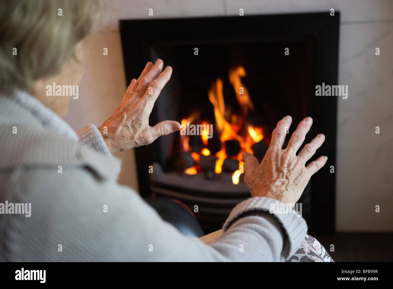 Ältere Frau Erwärmung Hände durch Feuer zu Hause Stockfoto