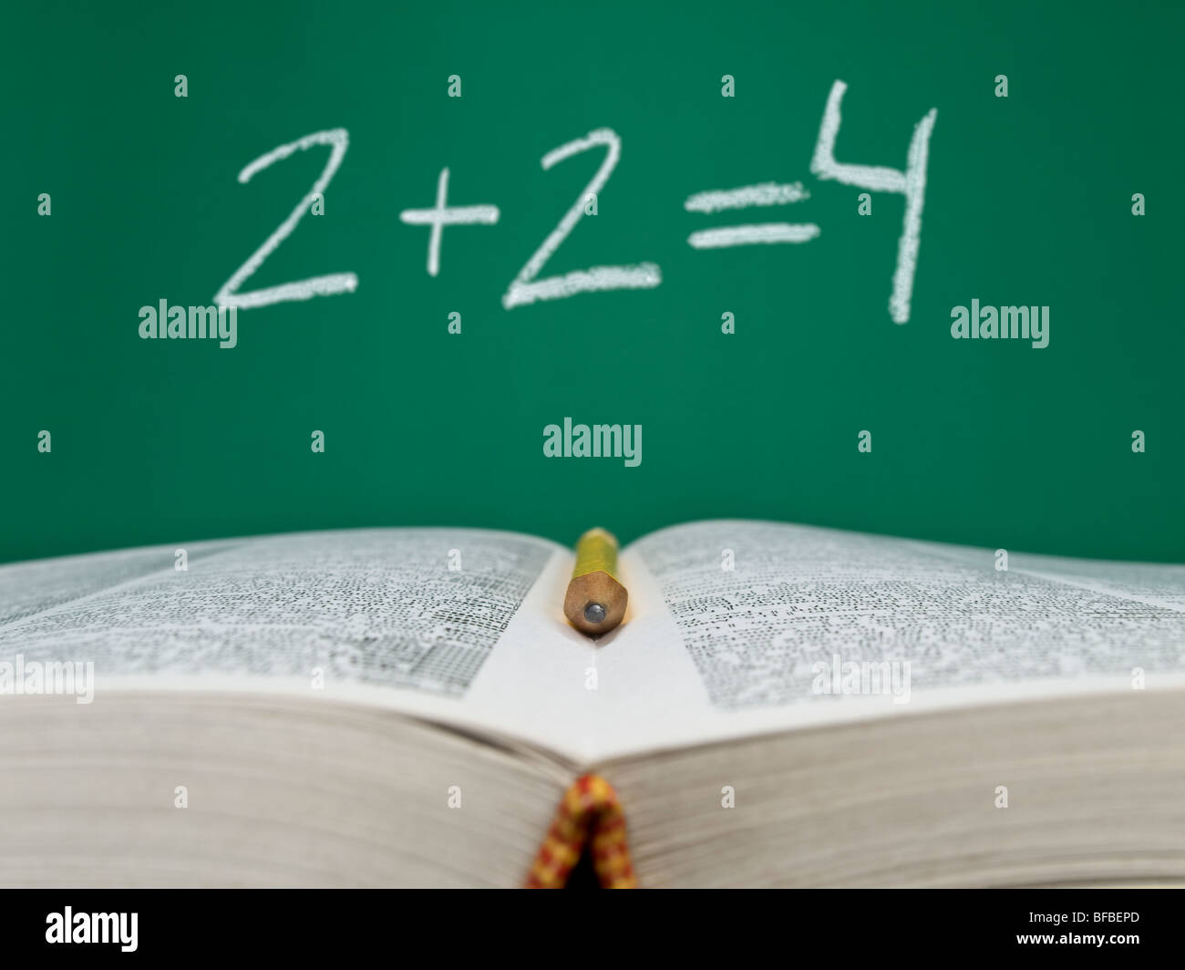 2 + 2 = 4 geschrieben auf einer Tafel mit Stift im Vordergrund und ein offenes Buch. Stockfoto