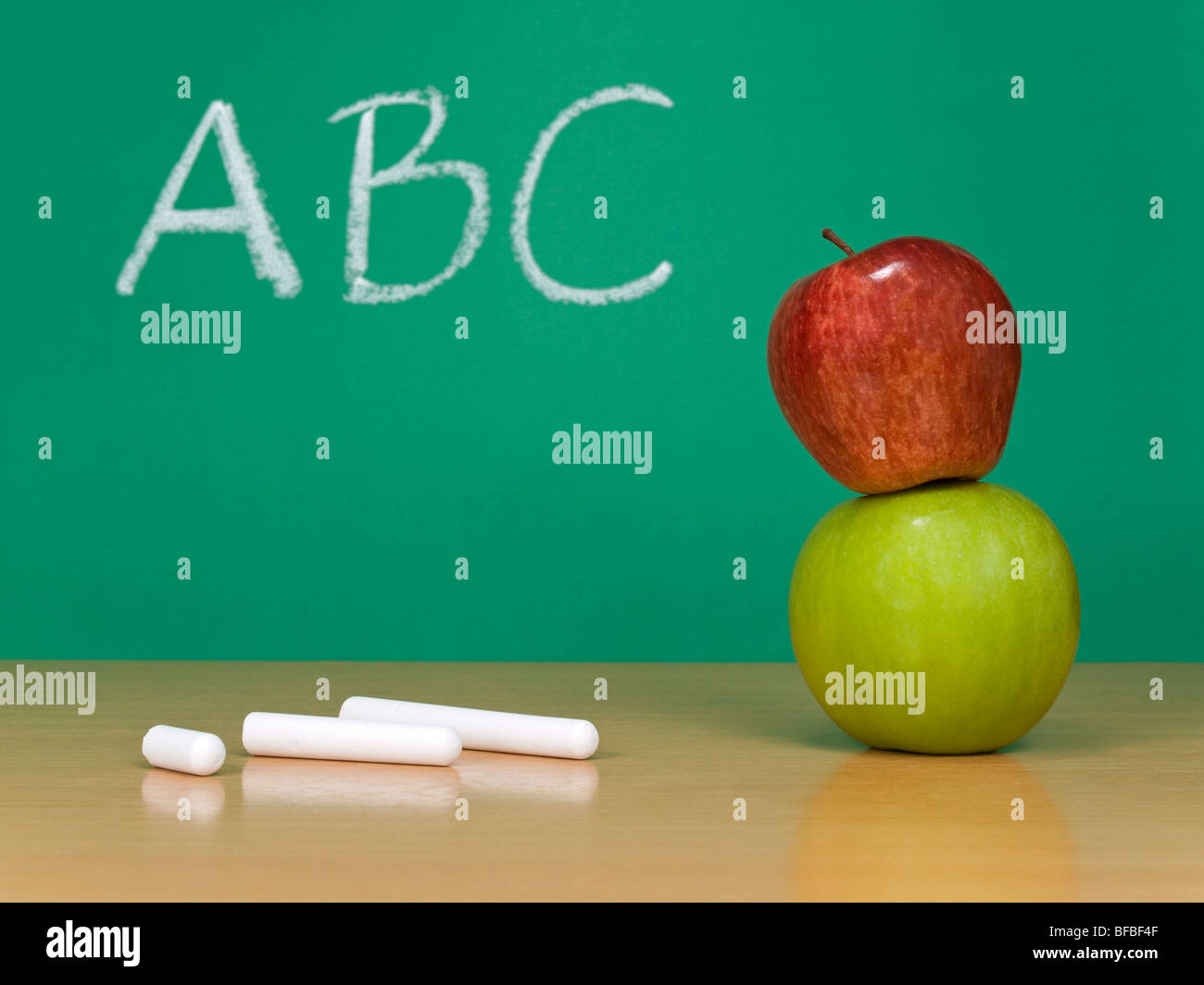 ABC auf einer Tafel geschrieben. Einige Kreiden und einen roten Apfel über eine grüne im Vordergrund. Stockfoto
