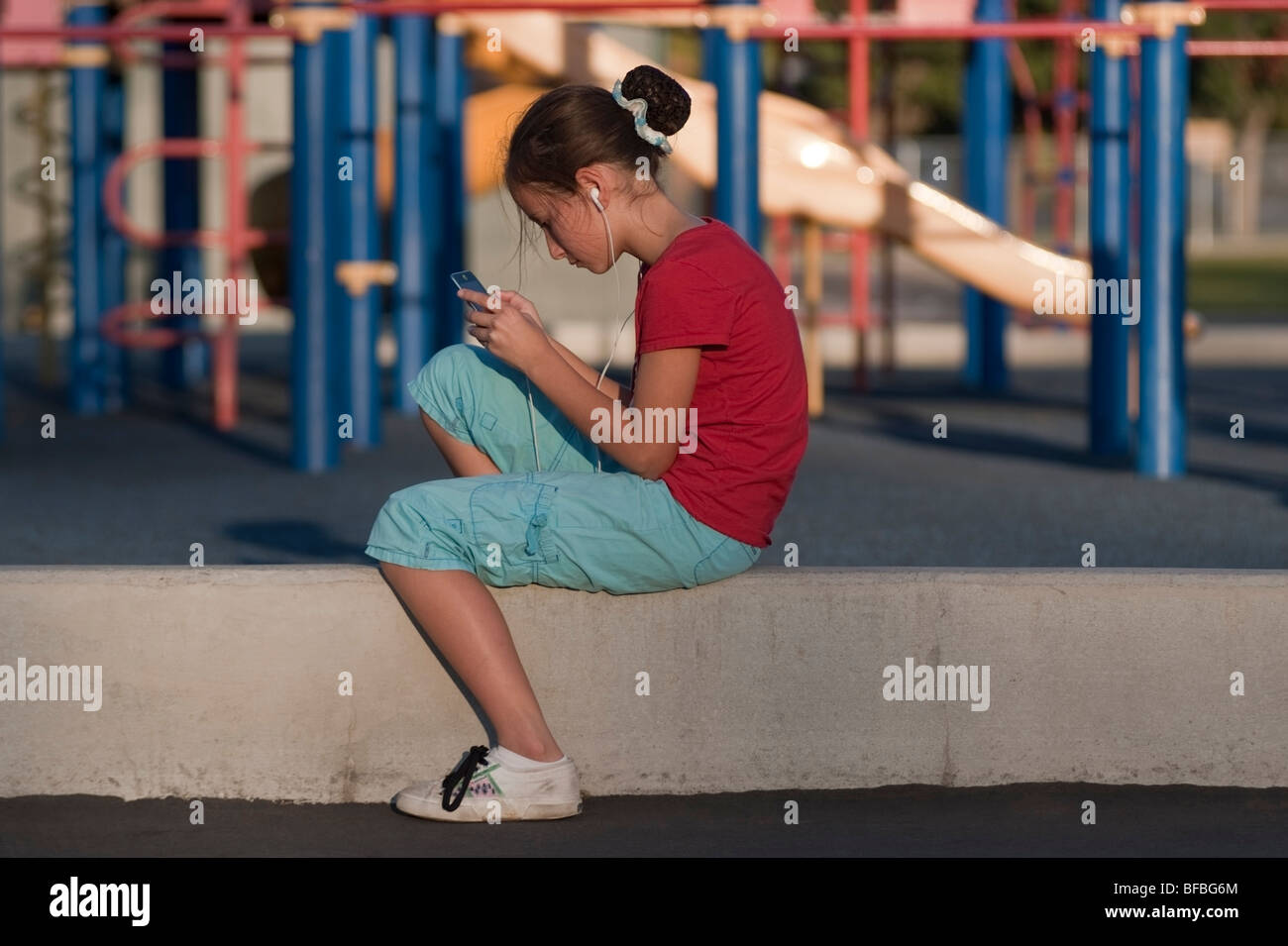 11 jähriges Mädchen spielt ein elektronisches Spiel auf ihrem iPod Touch auf dem Spielplatz eine Schule in der Nachbarschaft in San Jose, Kalifornien. Stockfoto