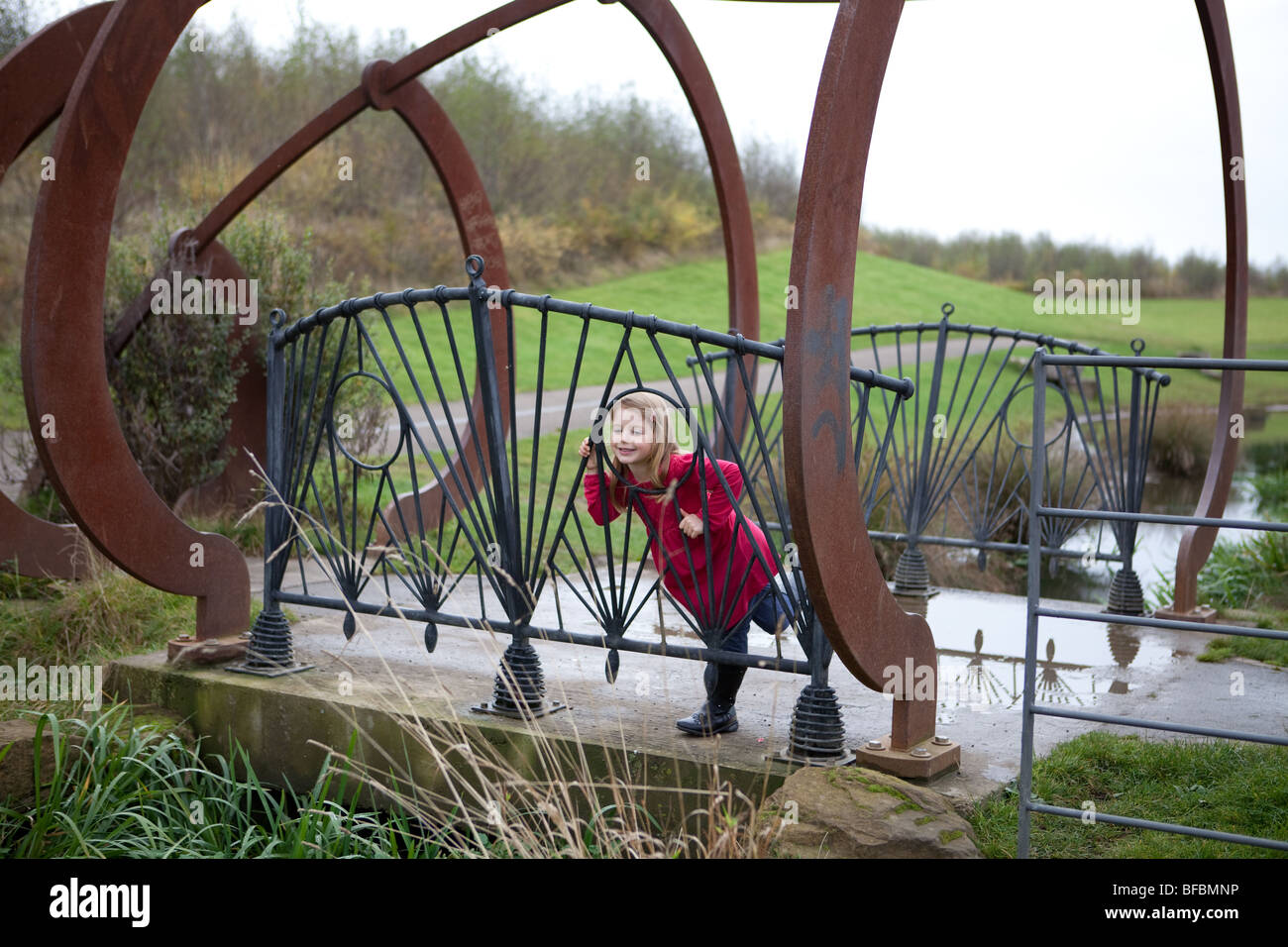 6 Jahre altes Mädchen in rosa Winterjacke auf eine Betonbrücke mit eisernen Schienen und rostigem Stahl Dekoration inmitten eines Parks Stockfoto