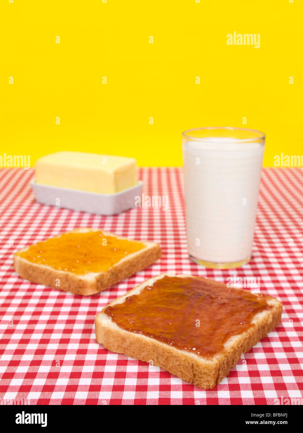 Zwei Scheiben Brot mit Marmelade, ein Glas Milch und ein Butter-Stick verteilt. Stockfoto