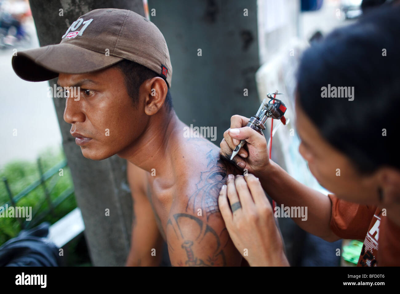 ein Künstler macht eine Tattoo für ein Mann auf der Straße in Blok M Bereich in Jakarta, Indonesien Stockfoto