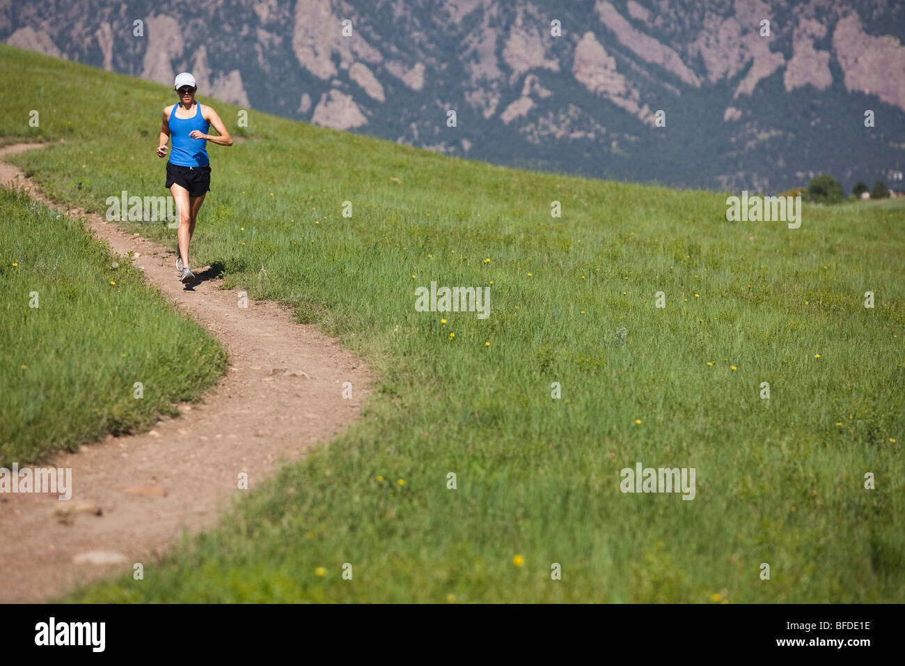 Eine Frau läuft auf die geschwungene Mesa Trail mit den Ausläufern im Hintergrund in der Nähe von Boulder, Colorado. Stockfoto