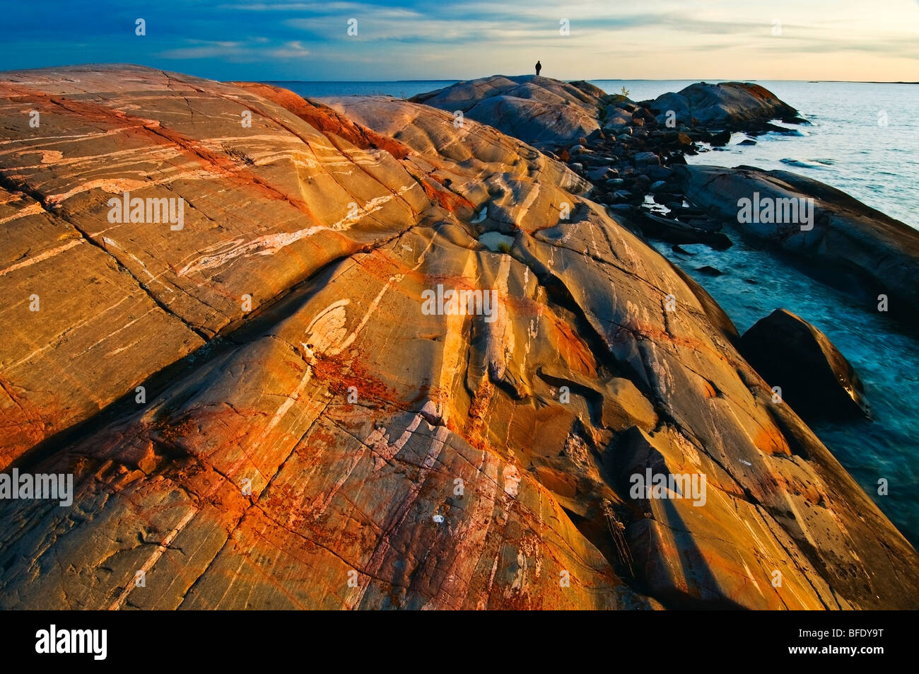 Mann im Hintergrund auf Pre-Kambrium Schild bei Sonnenuntergang an der Georgian Bay, südlich von Philip Edward Island, Ontario, Canada Stockfoto