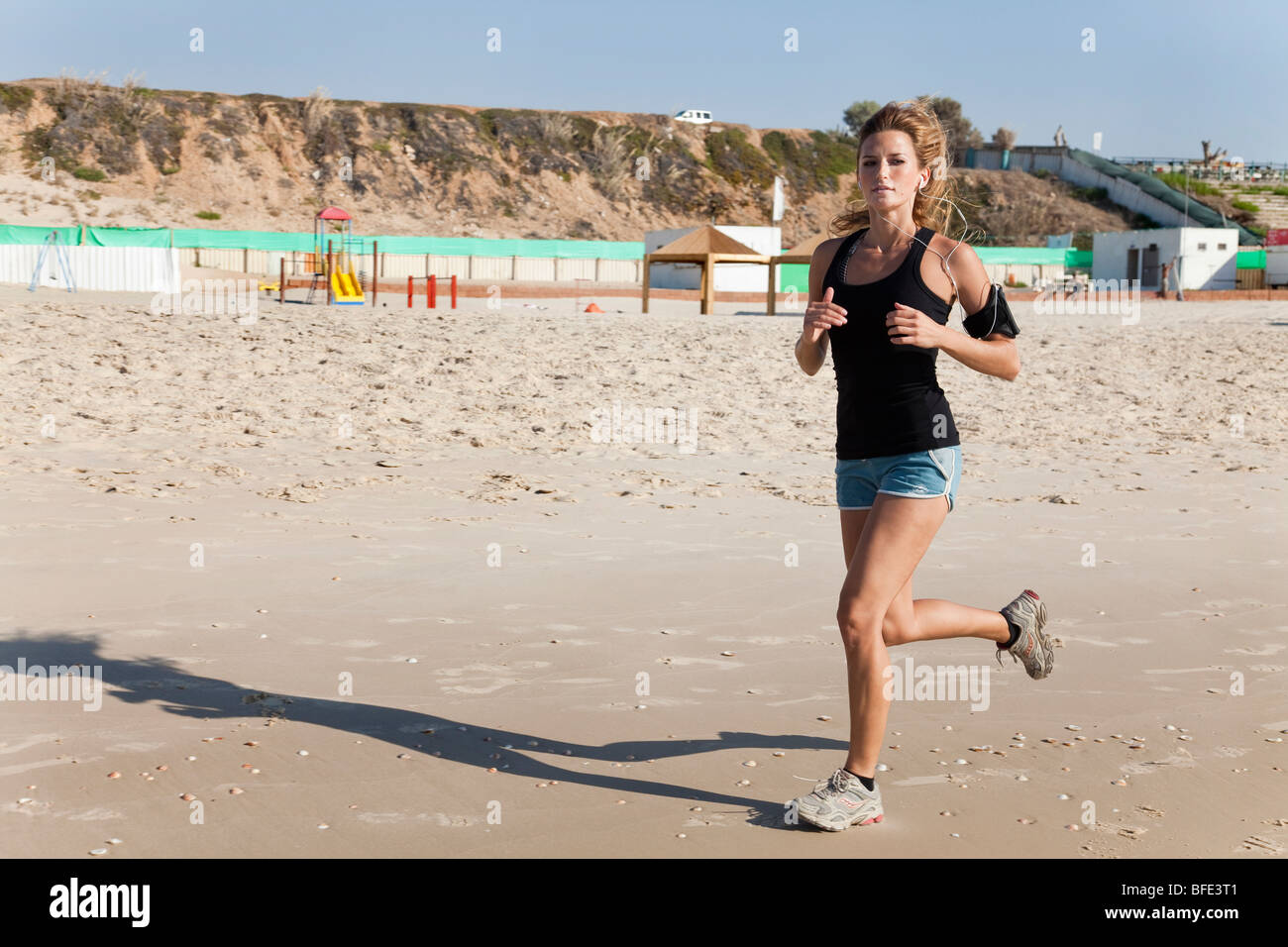 Junge Frau in ihren 20er Jahren joggt an einem Strand einen Musik-Player, befestigt an ihrem Arm - Model-Release verfügbar Stockfoto