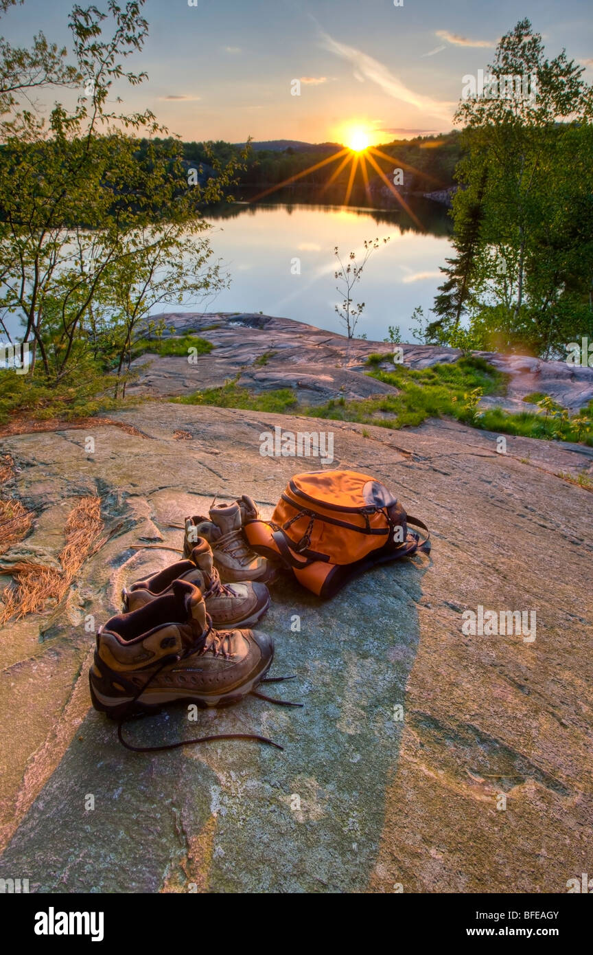 Wanderschuhe und Rucksack auf einem Felsen am Ufer des Lake George bei Sonnenuntergang in Killarney Provincial Park, Ontario, Kanada Stockfoto