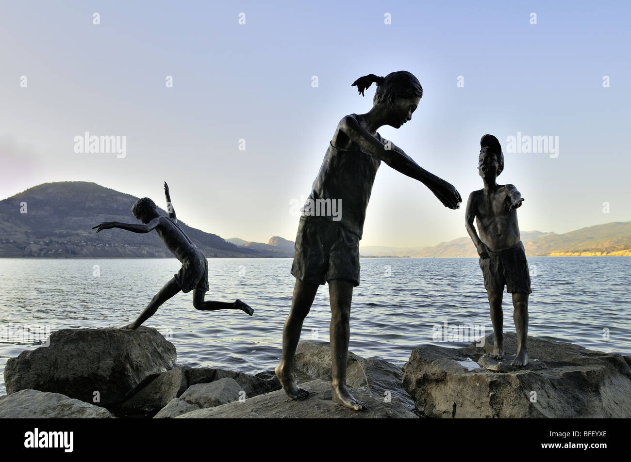 Statuen von Kindern spielen auf Felsen in der Nähe von Gewässerrand in Penticton, BC. Stockfoto