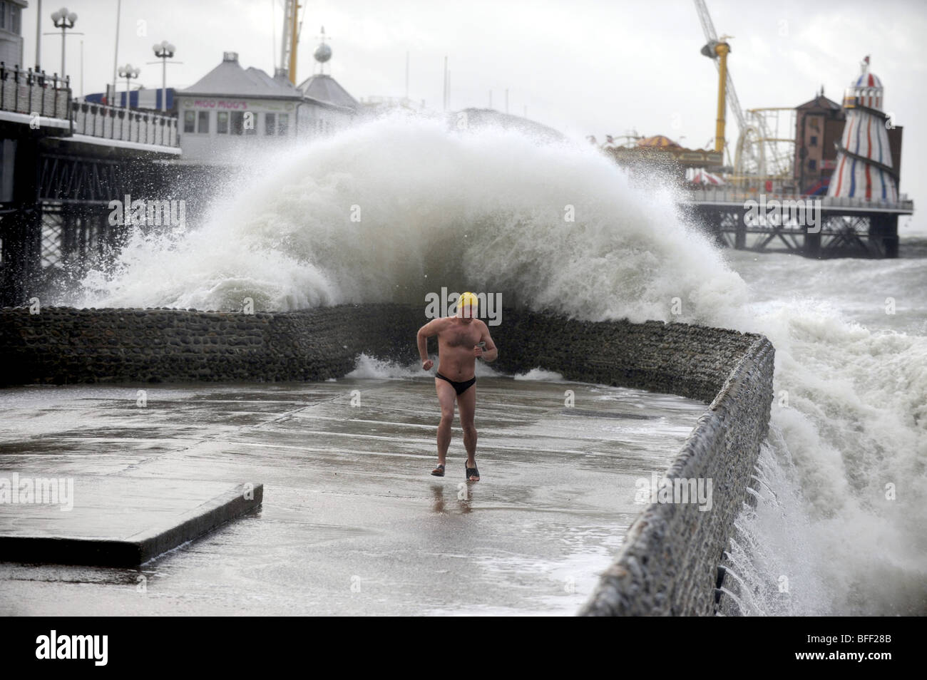 Adrian Bates, Mitglied des Brighton Swimming Clubs, tritt ausweichend ein, als eine riesige Welle an der Brighton Seafront UK 2009 über einen Groyne stürzt Stockfoto