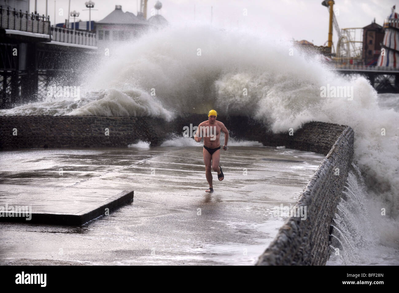 Adrian Bates, Mitglied des Brighton Swimming Clubs, tritt ausweichend ein, als eine riesige Welle an der Brighton Seafront UK 2009 über einen Groyne stürzt Stockfoto