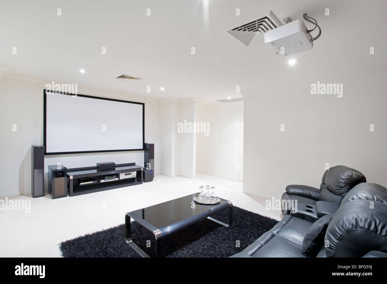 Heimkino-Raum mit schwarzen Ledersesseln liege, Projektor in Decke und Projektor-Bildschirm auf Wand. Stockfoto