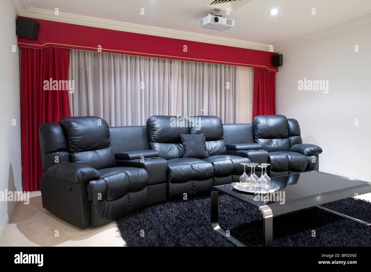 Heimkino-Raum mit schwarzen Ledersesseln liege, rote Vorhänge, schwarzen Teppich und Tisch mit Weingläsern Stockfoto