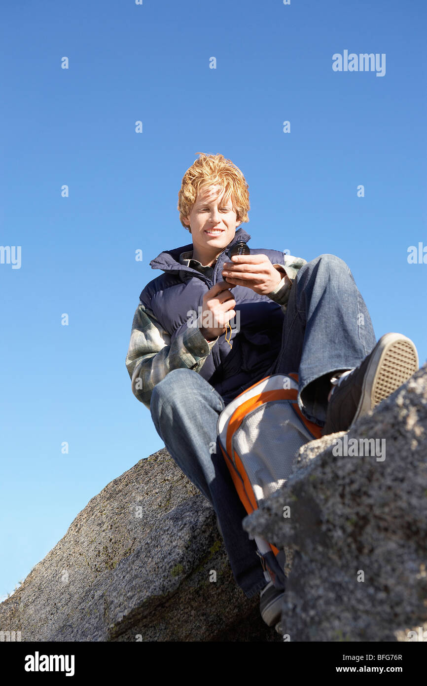 Junger Mann sitzt auf Felsbrocken, Kompaß, niedrigen Winkel Ansicht verwenden. Stockfoto