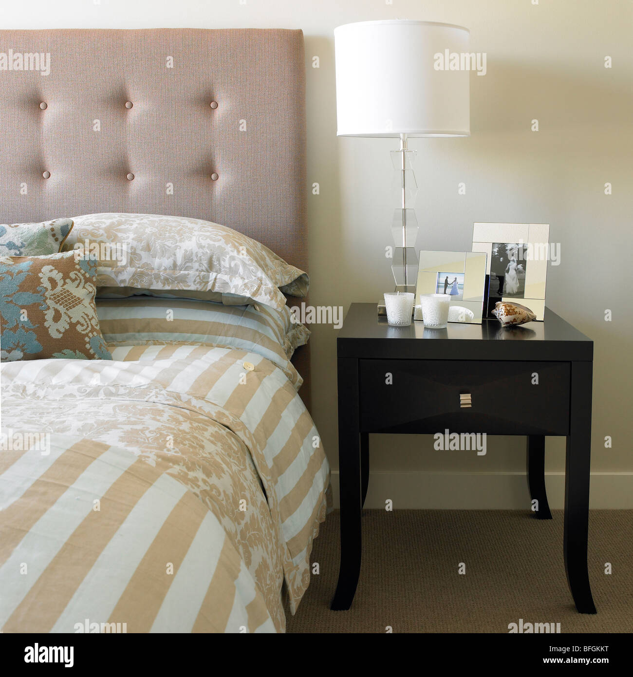 Bett mit Beistelltisch, Kerzen, Bilderrahmen und Lampe Stockfoto