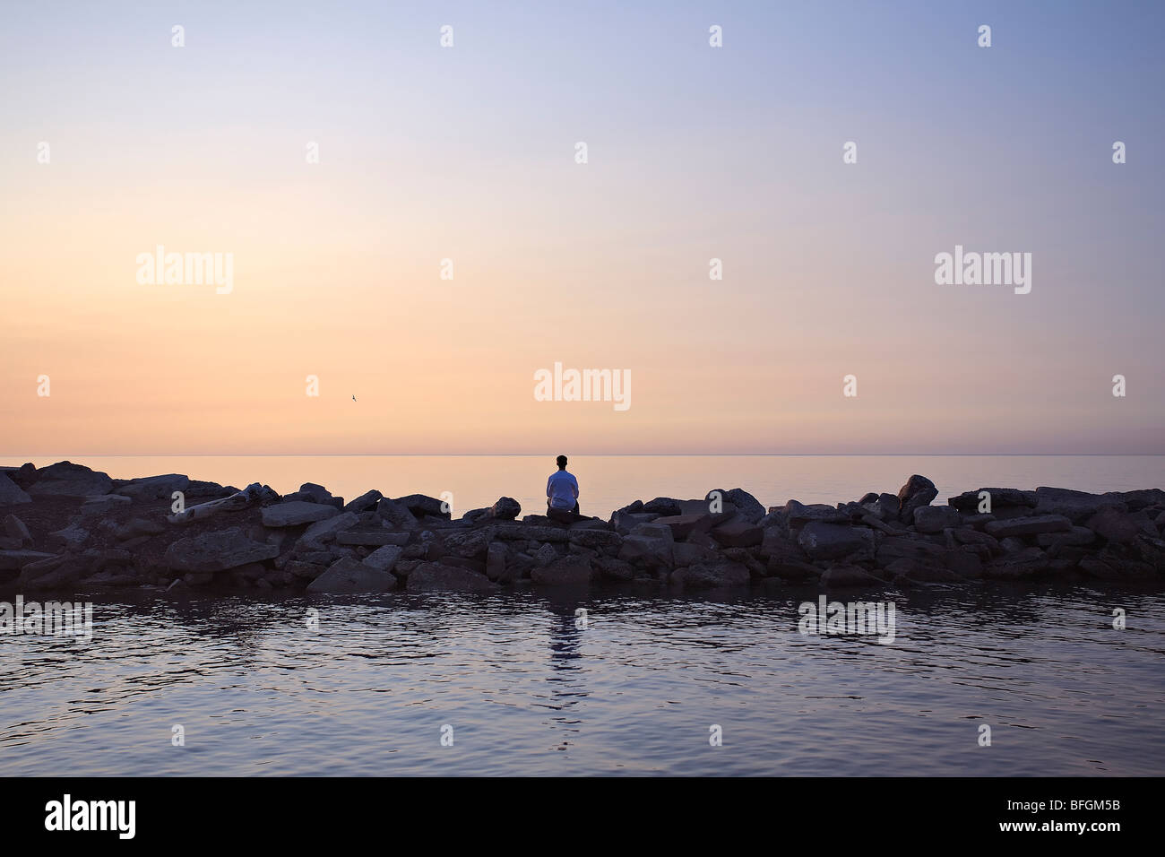 Mann sitzt auf Wellenbrecher bei Sonnenaufgang, Lake Ontario, Woodbine Strand, Toronto, Ontario Stockfoto