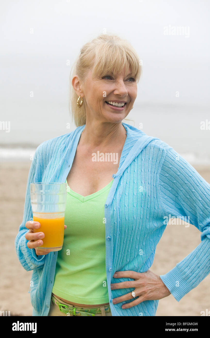 Mid-Adult-Frau am Strand mit einem Glas Orangensaft Stockfoto