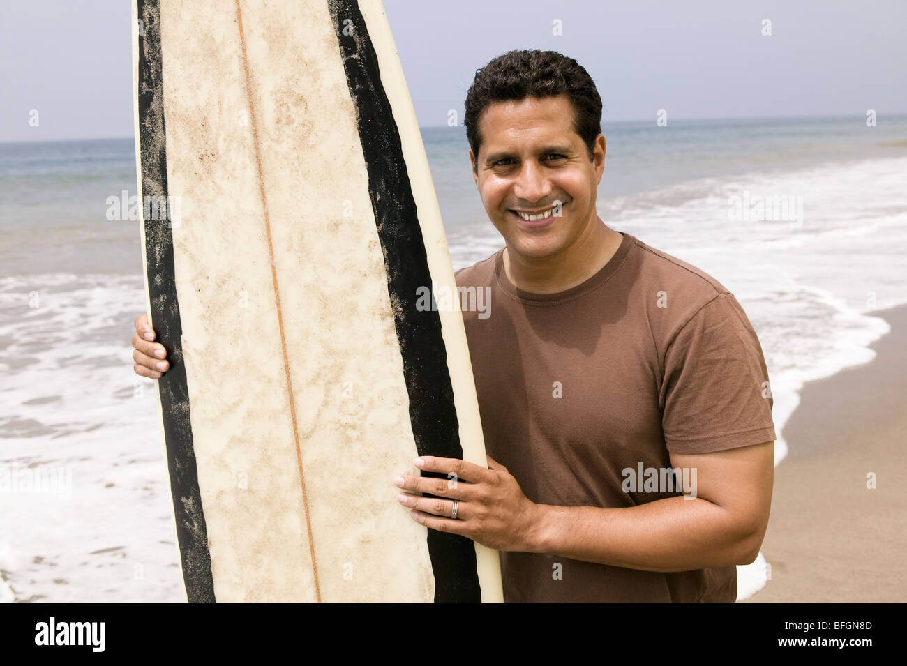 Porträt des Mannes mit Surfbrett am Strand Stockfoto