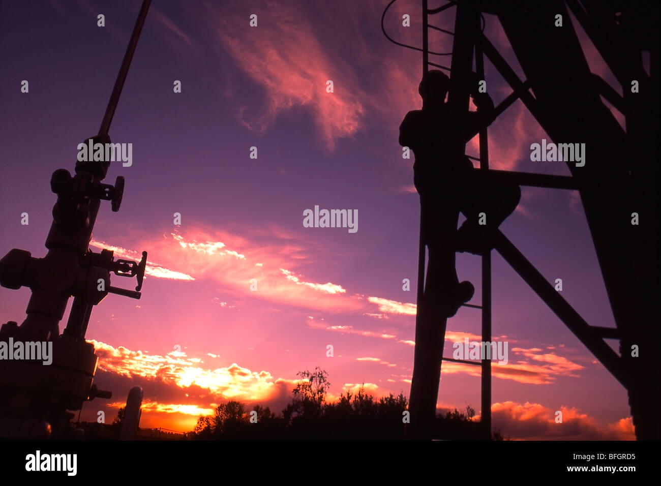 Öl-Industrie Arbeiter Klettern Pumpe Jack in Alberta, Kanada, bei Sonnenuntergang. Stockfoto
