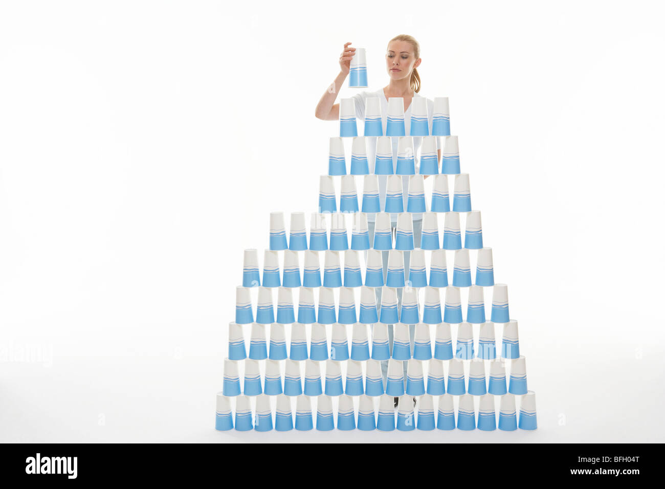 Frau Stapeln Plastikbecher in Pyramide vor weißem Hintergrund Stockfoto