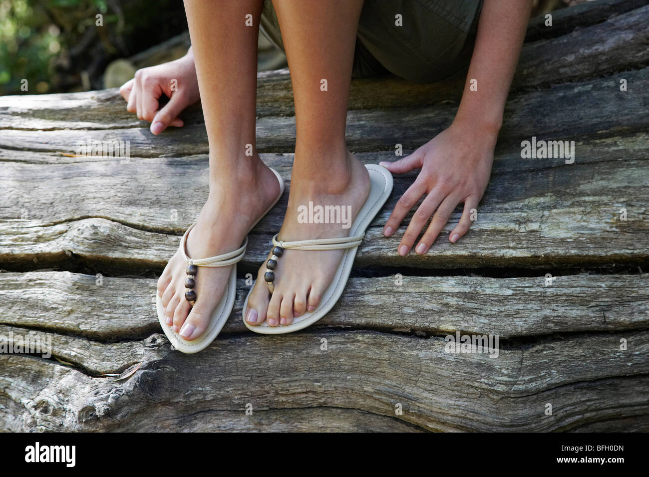 Teenager-Mädchen (16-17 Jahre) tragen Flip-flops sitzend auf Baumstamm, niedrige Abschnitt Stockfoto