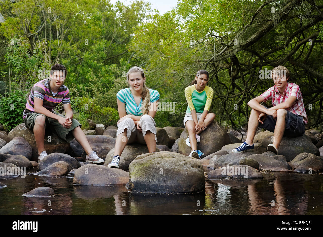 Porträt von vier Jugendliche (16-17 Jahre) sitzt auf Steinen durch Fluss Stockfoto