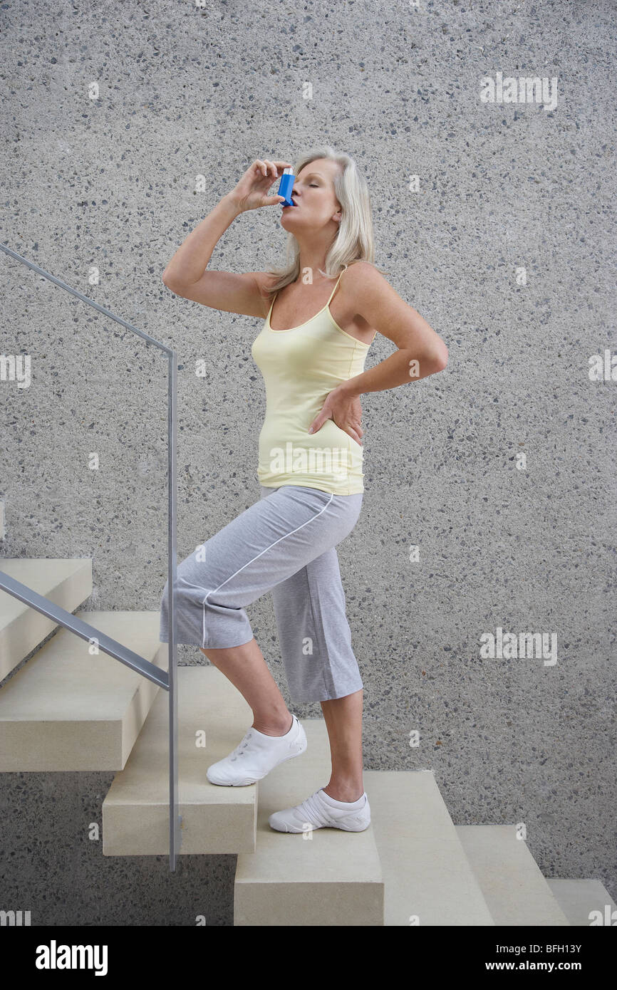 Reife Frau stehend, hand auf die Hüfte, auf Treppen, mit Inhalator, Seitenansicht Stockfoto
