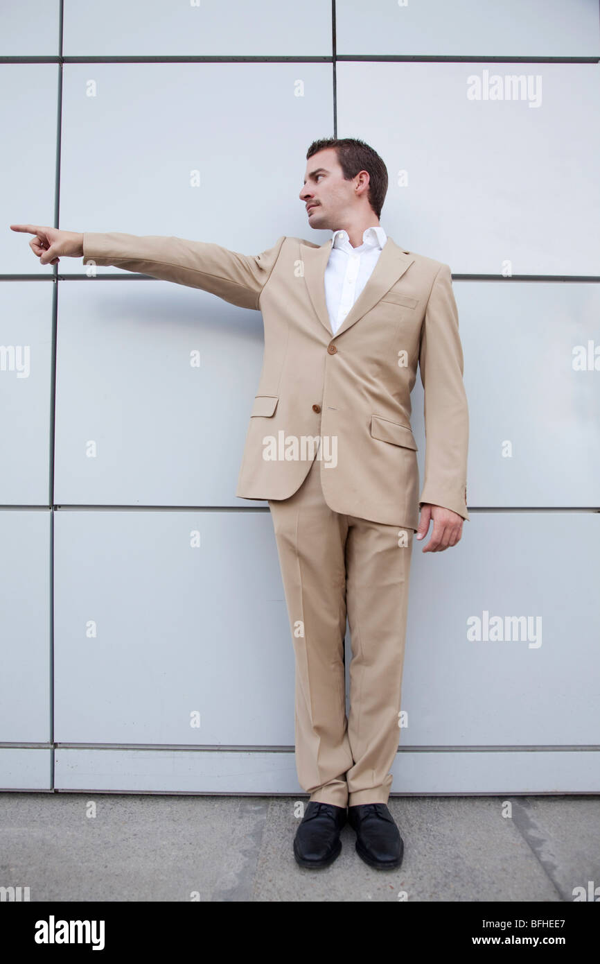 junger Mann im Anzug gegen eine Wand zeigen Stockfoto