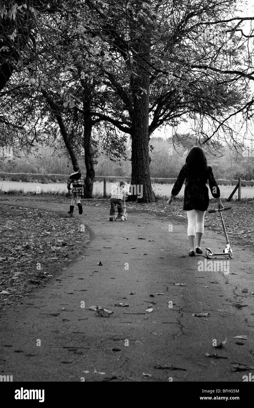 Drei kleine Kinder zu Fuß entlang eines Pfades im Herbst auf ihre Roller zu spielen. Stockfoto