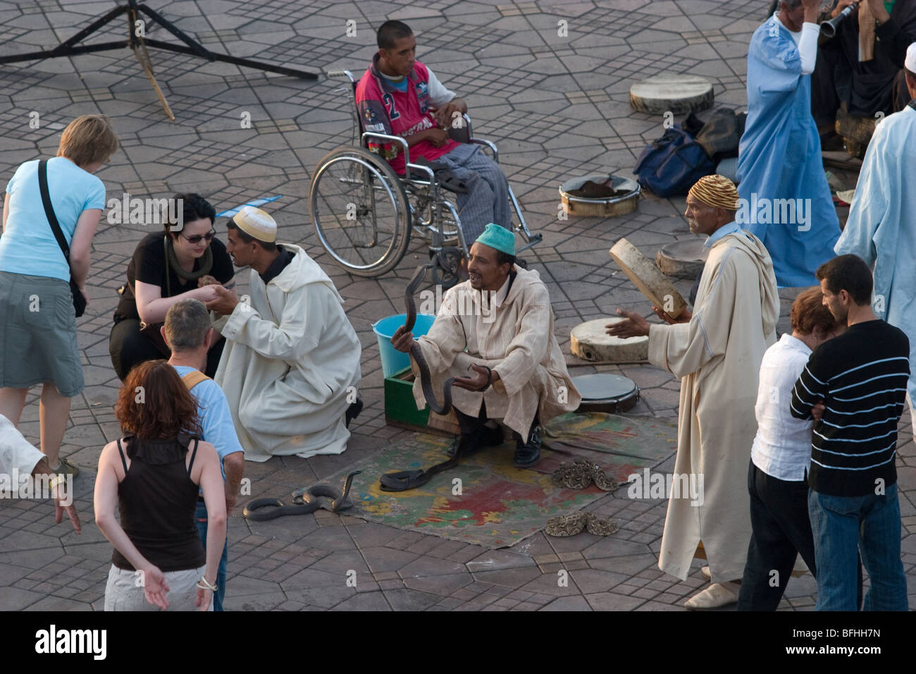 Touristen mischen sich mit Schlangenbeschwörer auf Djemaa el-Fna, dem zentralen Platz in Marrakesch, heute ein UNESCO-Weltkulturerbe Stockfoto