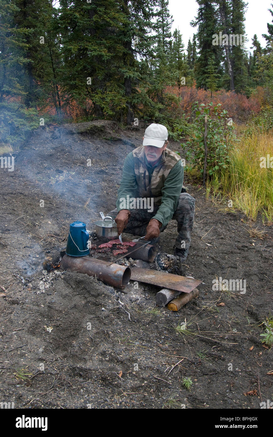 Mann im Freien essen im Camp auf improvisierten Grill vorbereiten. Yukon Territorium, Kanada. -Modell veröffentlicht. Stockfoto