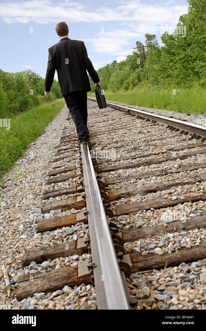 Mittleres Alter Geschäftsmann zu Fuß auf Schiene-Straße-Linie mit dem Aktenkoffer in der hand. Stockfoto