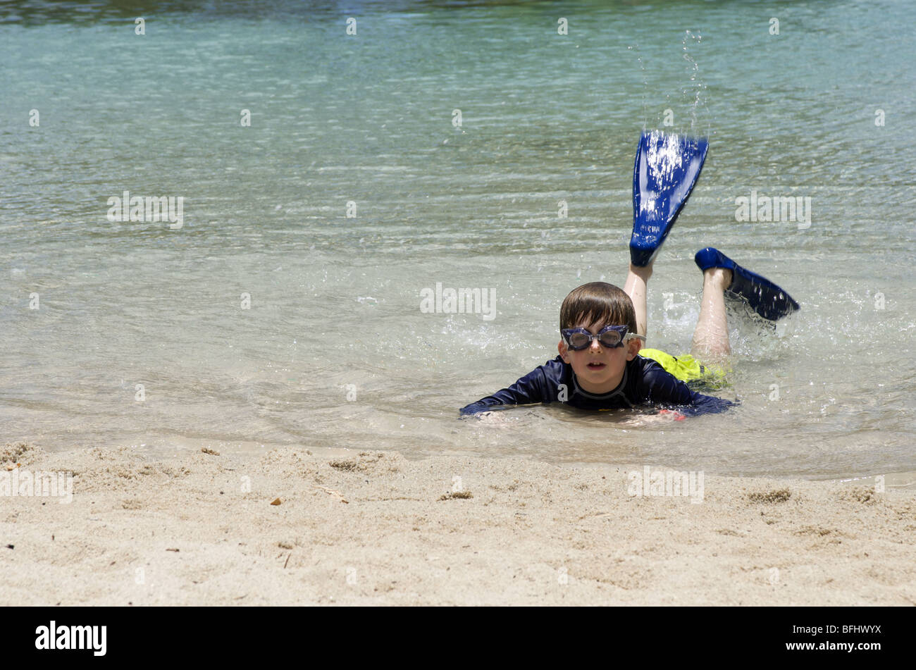 Boy spritzt mit Flossen auf Strand Stockfoto
