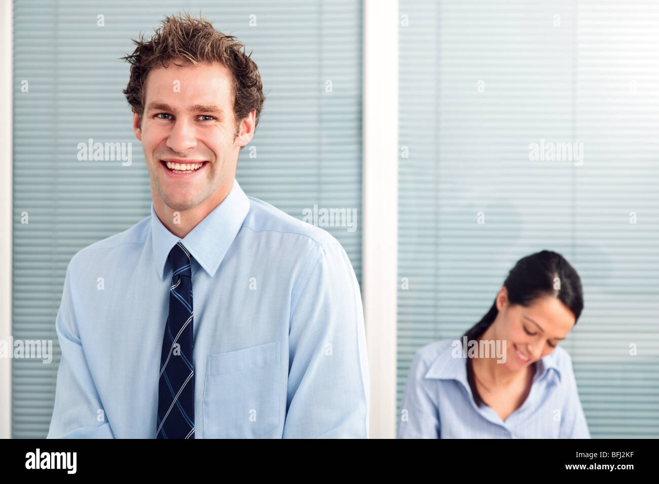 Geschäftsmann in einem Büro lächelnd zu Kamera, Kollegin im Hintergrund unscharf. Stockfoto