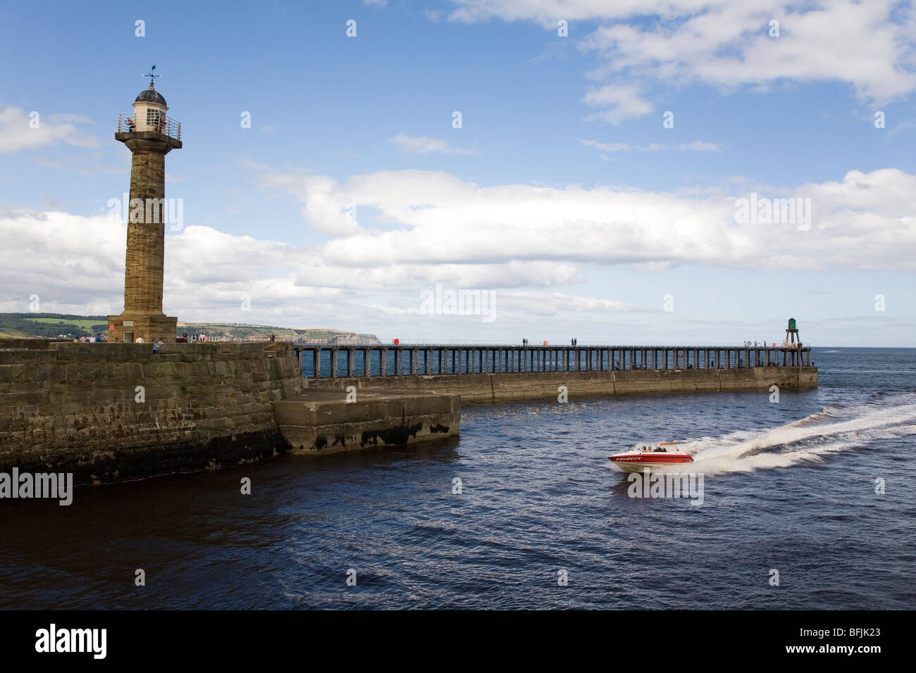 Ein Motorboot navigiert den alten steinernen Leuchtturm an der West Pier von Whitby in North Yorkshire, England. Stockfoto