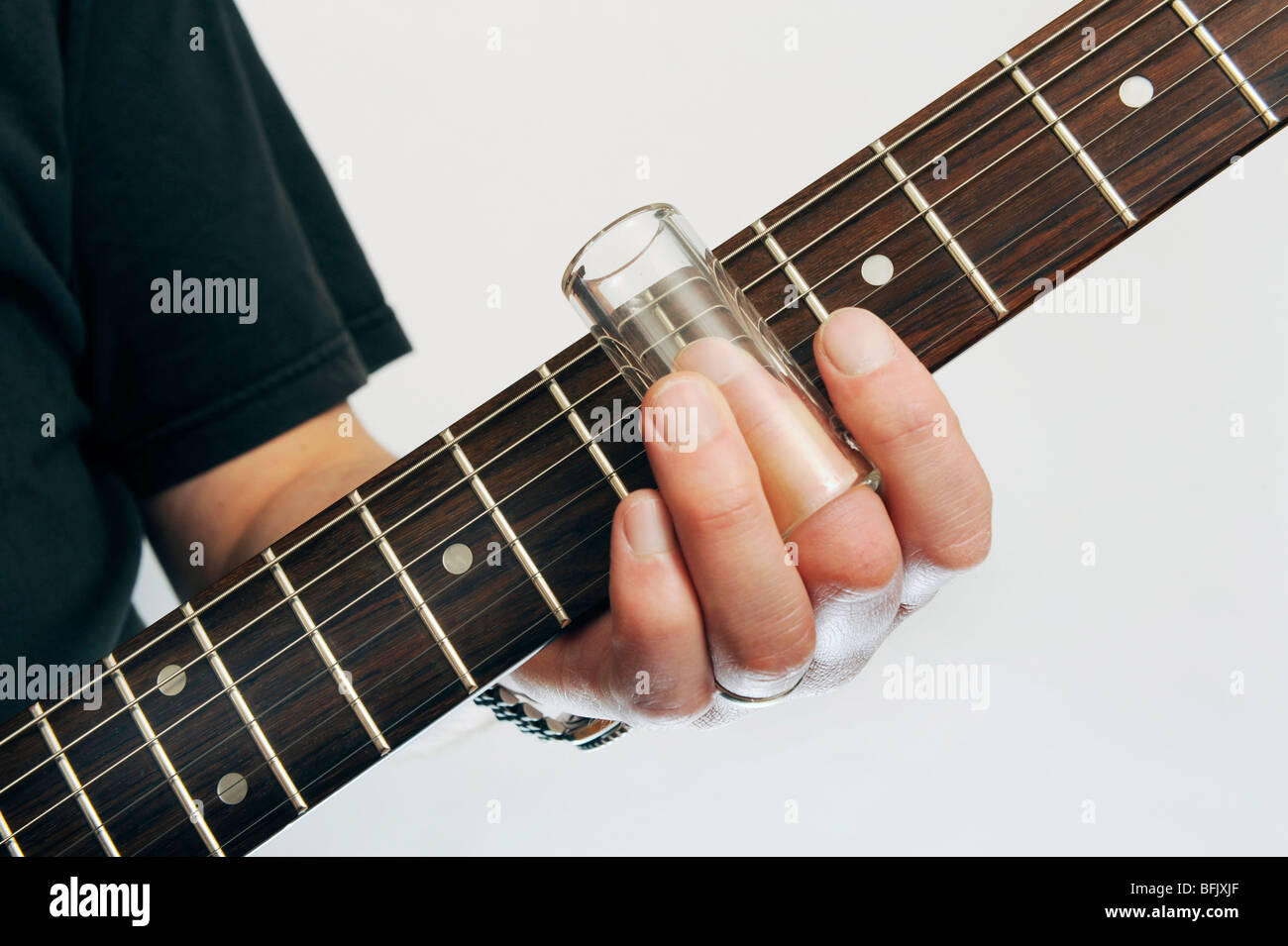 ein mans Hand zeigt einen Flasche Hals Objektträger Gitarre gegen einen Gitarrenhals Stockfoto