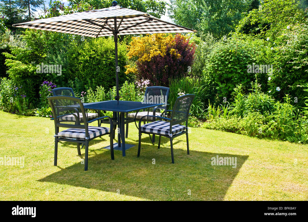 Gartenmöbel und Sonnenschirm auf einer Wiese in einem typisch englischen Stadt oder Land festgelegten Garten im Sommer Stockfoto