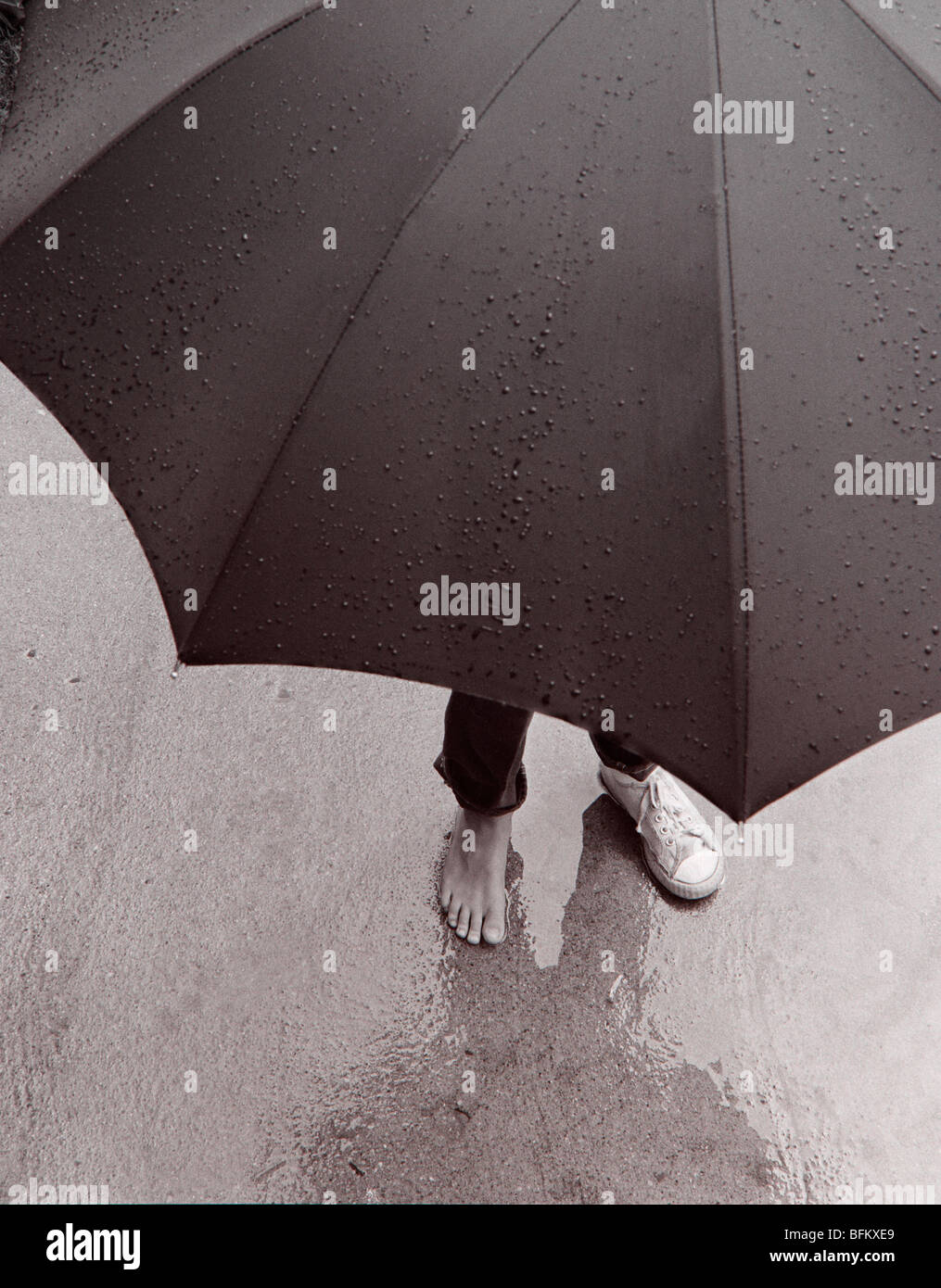 Person steht im Regen mit Regenschirm Stockfoto