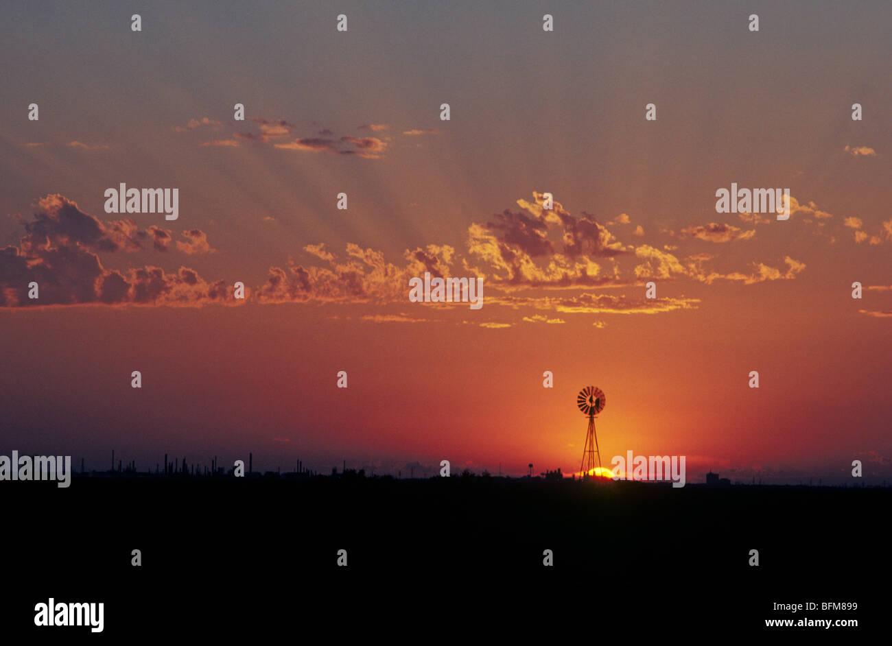 Eine Windmühle steht in der Nähe einer Ölraffinerie bei Sonnenuntergang in Odessa, Texas Panhandle Stockfoto