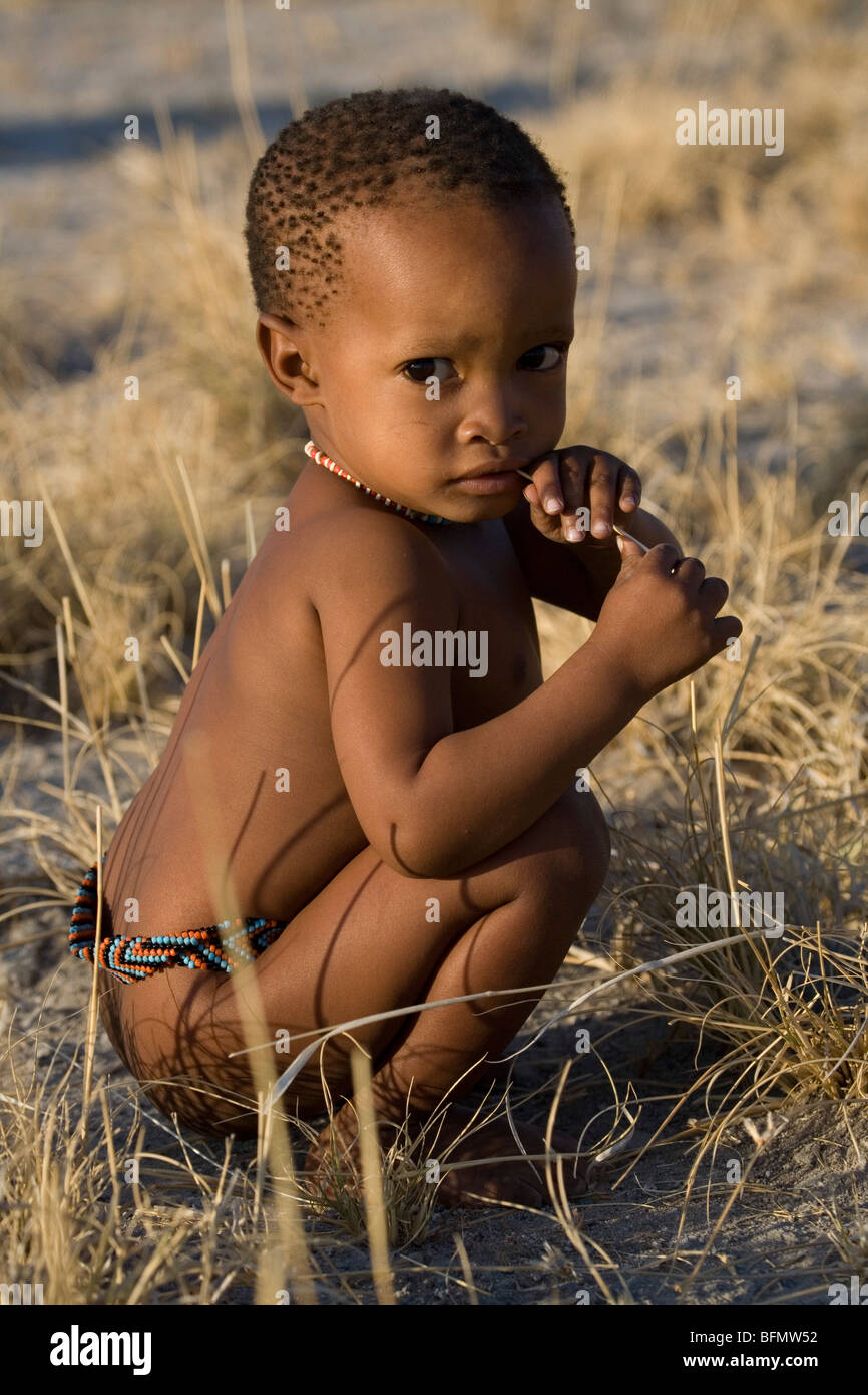 Botswana, Makgadikgadi. Ein San Bushman Baby spielt in Trockenrasen, tragen nur einen traditionellen Gürtel aus Perlen. Stockfoto