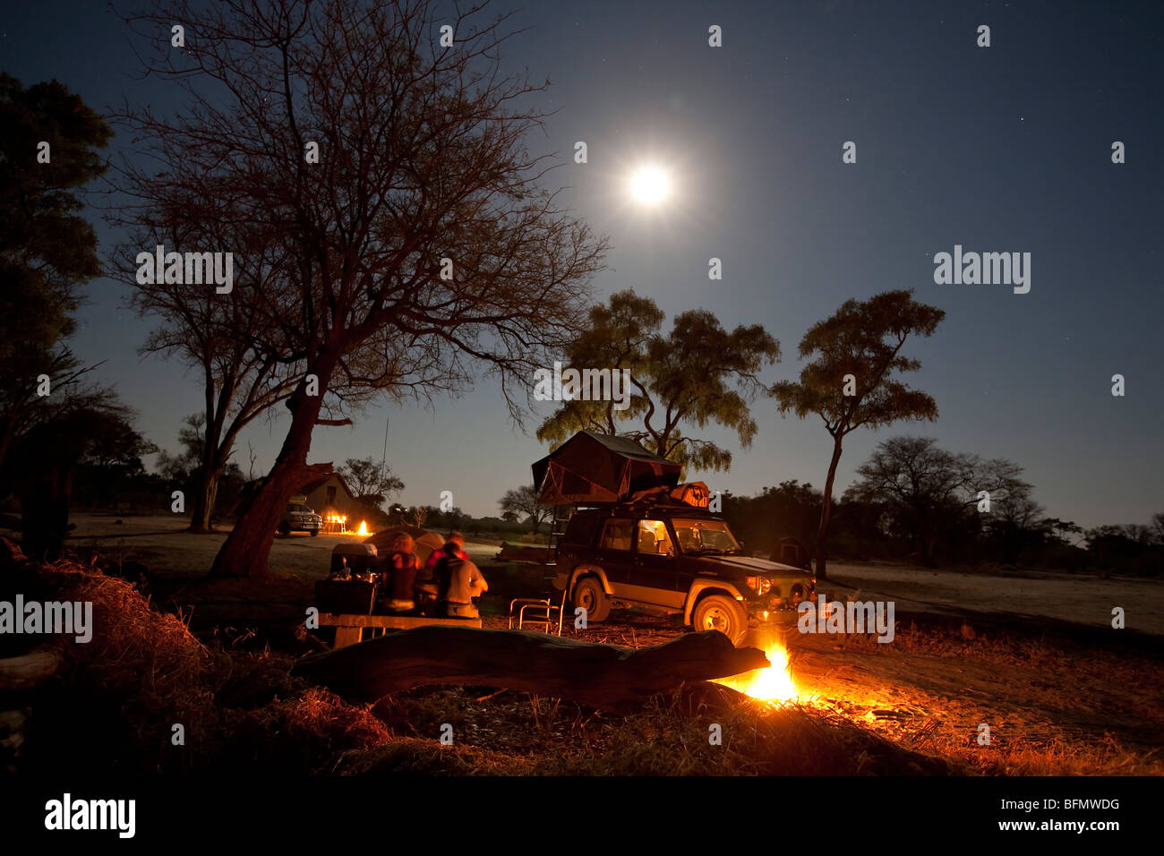 Botswana, Savuti. Eine Familie genießt ihre Mahlzeit durch das Feuer, mit der Expedition 4 x 4 im Hintergrund. Stockfoto