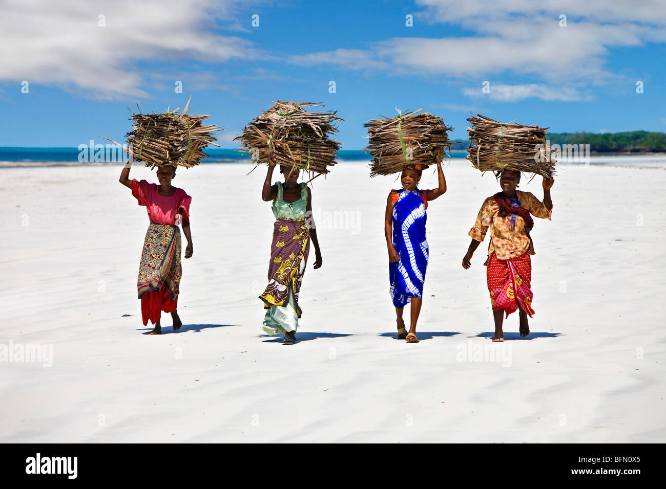 Kenia, Mombasa. Frauen tragen auf ihren Köpfen Makuti (getrocknete Kokosnuss Palmwedel als Dachmaterial verwendet) an einem Strand. Stockfoto