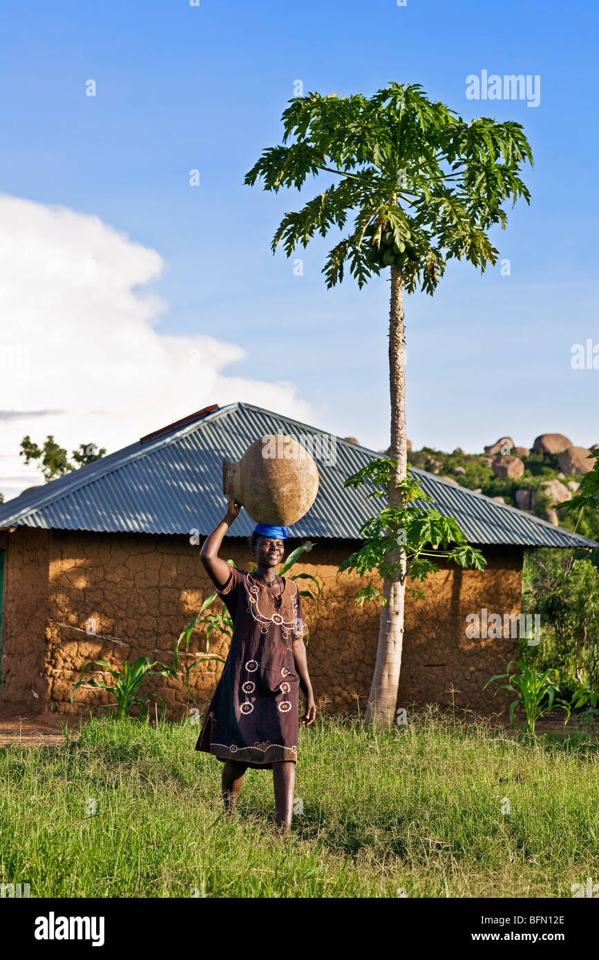 Kenia, Nyanza Bezirk.  Eine Luo Frau trägt ein großes Wasserreservoir zu ihrem Haus in der Nähe von Kit Mikayi Stockfoto