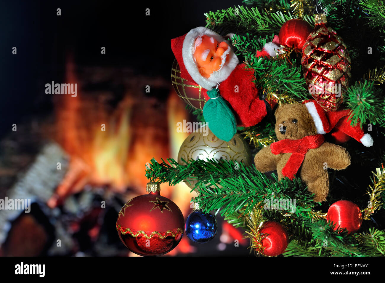 Weihnachtsmann und Glocken hängen im Baum vor Herd / Kamin Stockfoto