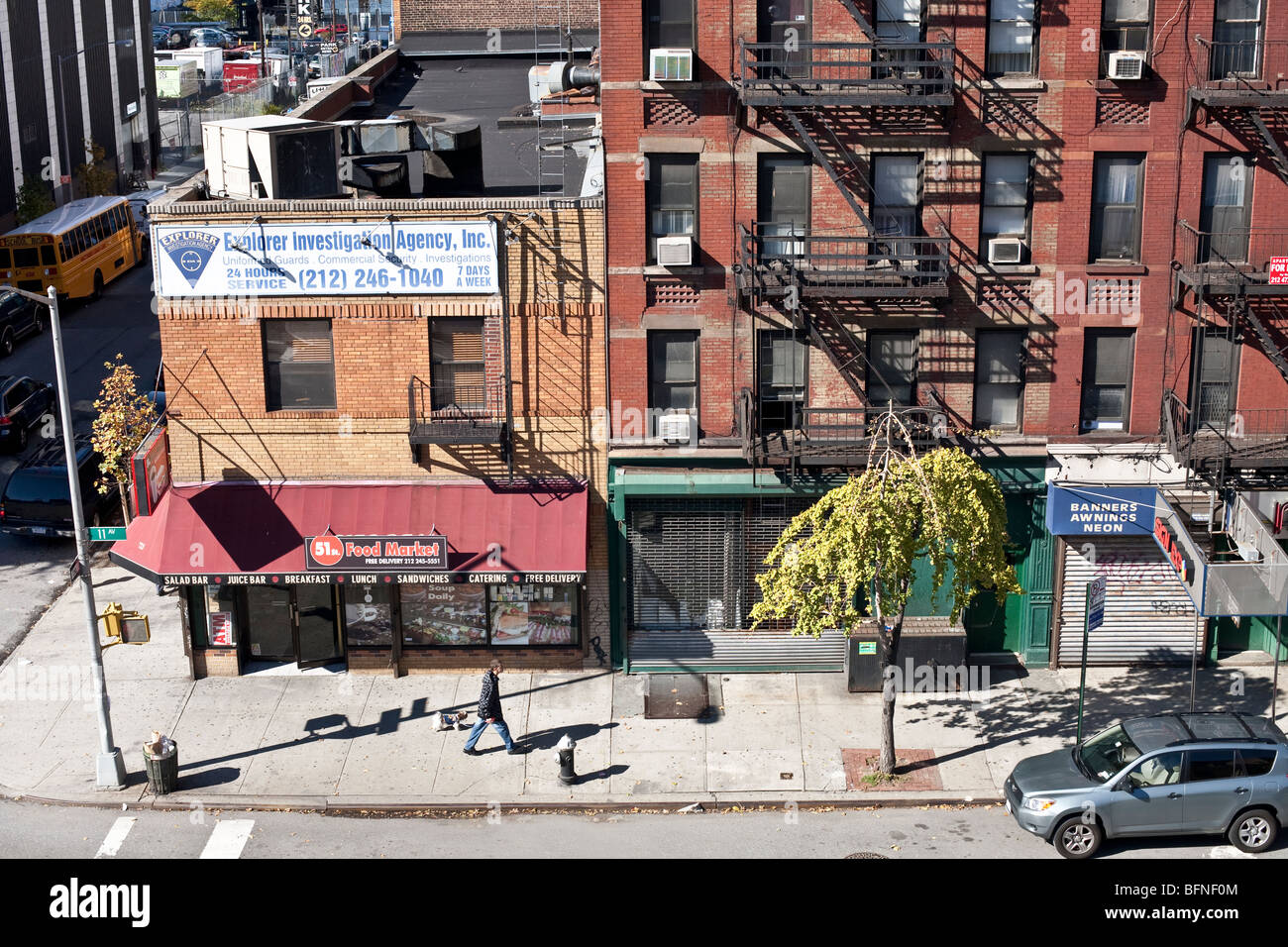 Blick hinunter auf die Ecke Deli verkümmert Bürgersteig Baum & Hund Walker & alten roten Backsteinfassaden Mietshaus auf eine brillante Herbst Sonntag Stockfoto