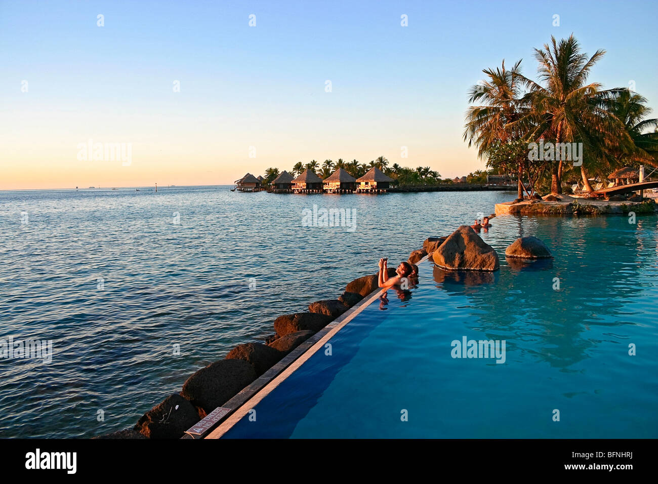 Menschen beobachten Sonnenuntergang beim schweben im Schwimmbad am Rande des Ozeans im romantischen Luxus-Resort in Papeete, Tahiti Stockfoto